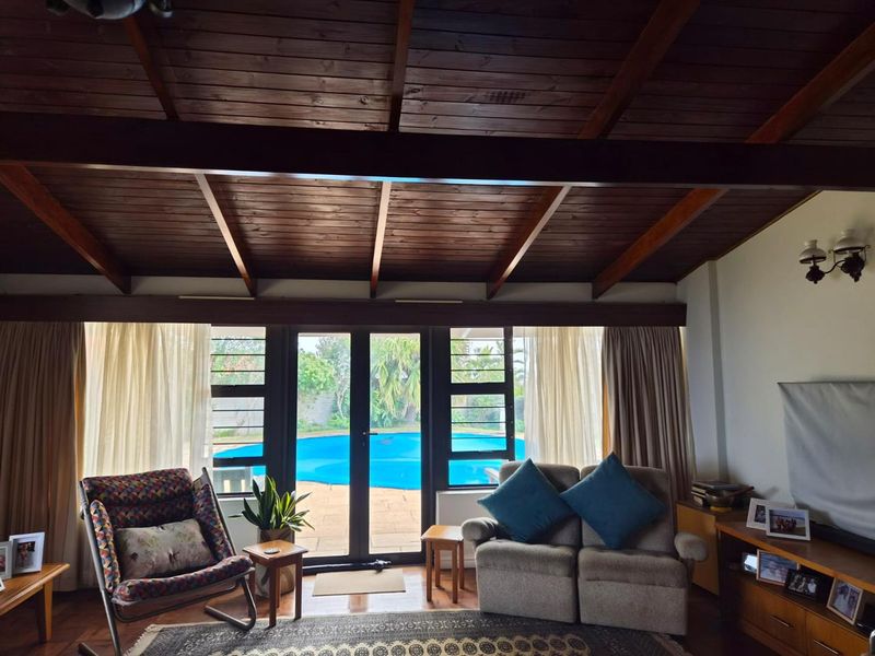 A cozy living room featuring a vaulted timber beam ceiling and large glass doors providing direct access to the outdoor pool area.