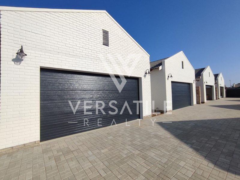 A row of modern townhouse garages featuring white painted brick facades, dark sectional doors, and neat paved driveway access.