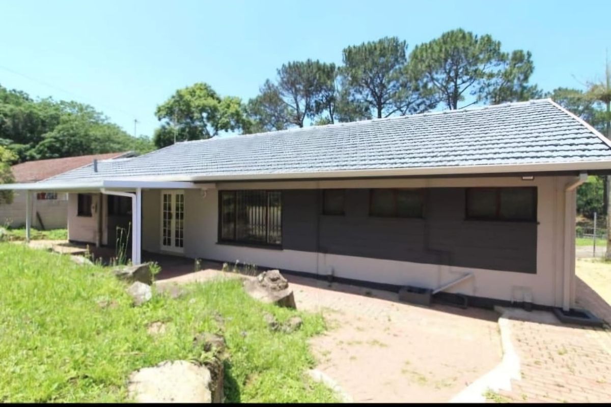 Rear view of the house featuring a tiled roof, covered patio area, and paved pathways leading to the garden.