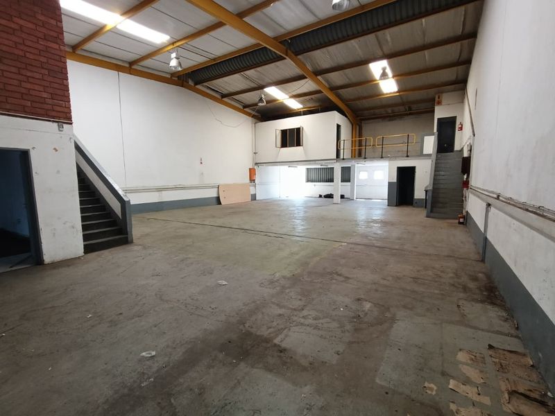 Spacious industrial warehouse unit featuring high ceilings with exposed steel trusses, a mezzanine level, and concrete flooring, suitable for various commercial or storage uses.