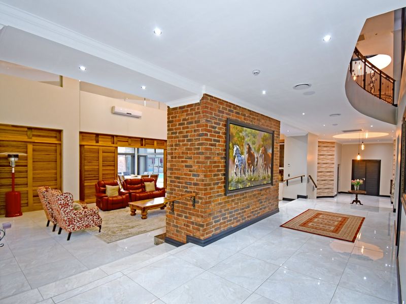 Spacious open-plan living area featuring a prominent exposed brick wall, polished tile flooring, recessed lighting, and an elegant curved staircase with wrought iron detailing.