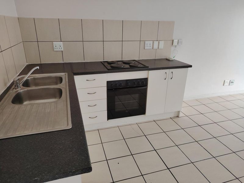 A functional kitchen featuring built-in cabinetry, a double bowl stainless steel sink, an integrated oven and hob, and neutral tiled flooring.