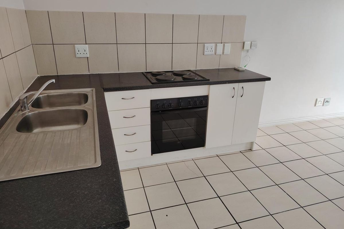 A functional kitchen featuring built-in cabinetry, a double bowl stainless steel sink, an integrated oven and hob, and neutral tiled flooring.