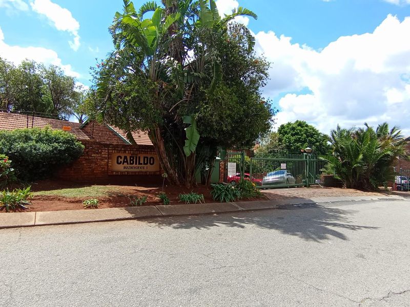 Street view of the Cabildo complex entrance, featuring a brick boundary wall, secure gated access, and established landscaping.