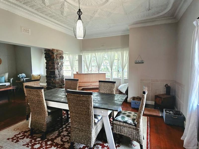 Spacious dining room featuring a striking ornate pressed metal ceiling, hardwood flooring, and a characterful stone fireplace column with a wood-burning stove.