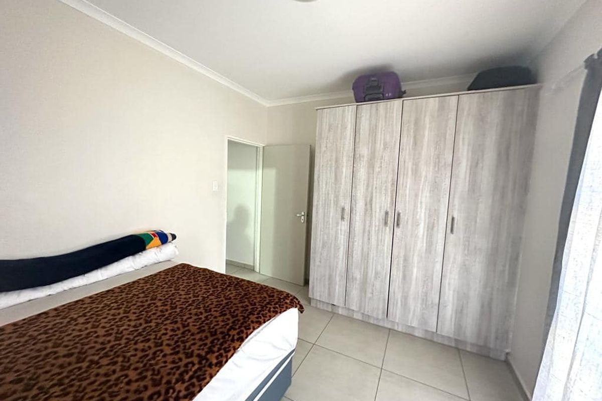 A bedroom featuring light-toned tiled flooring and a large, built-in wardrobe with a wood-grain finish.