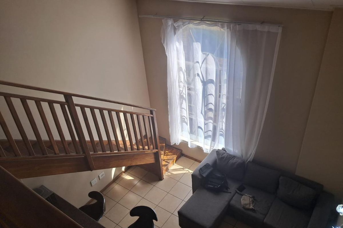 A double-volume living area featuring a wooden staircase, tiled flooring, and a large window allowing for natural light.