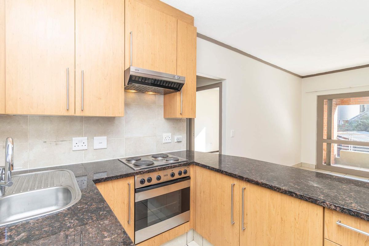 A functional kitchen featuring light wood cabinetry, dark granite countertops, a built-in oven, electric hob, and stainless steel extractor fan.
