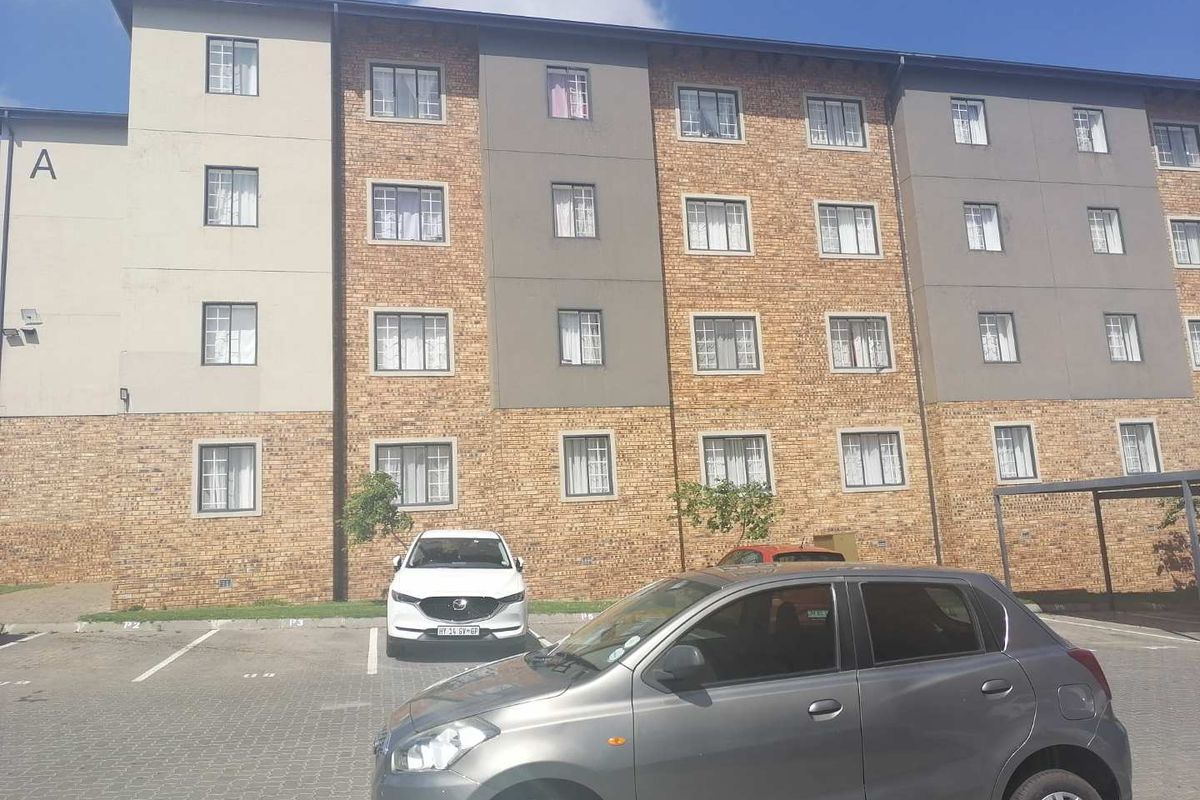 Front elevation of a multi-story townhouse complex featuring a brick and rendered facade with dedicated paved parking bays.