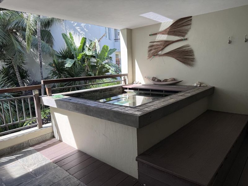 A covered balcony featuring a built-in plunge pool with tiled surround and timber decking, overlooking lush tropical garden greenery.