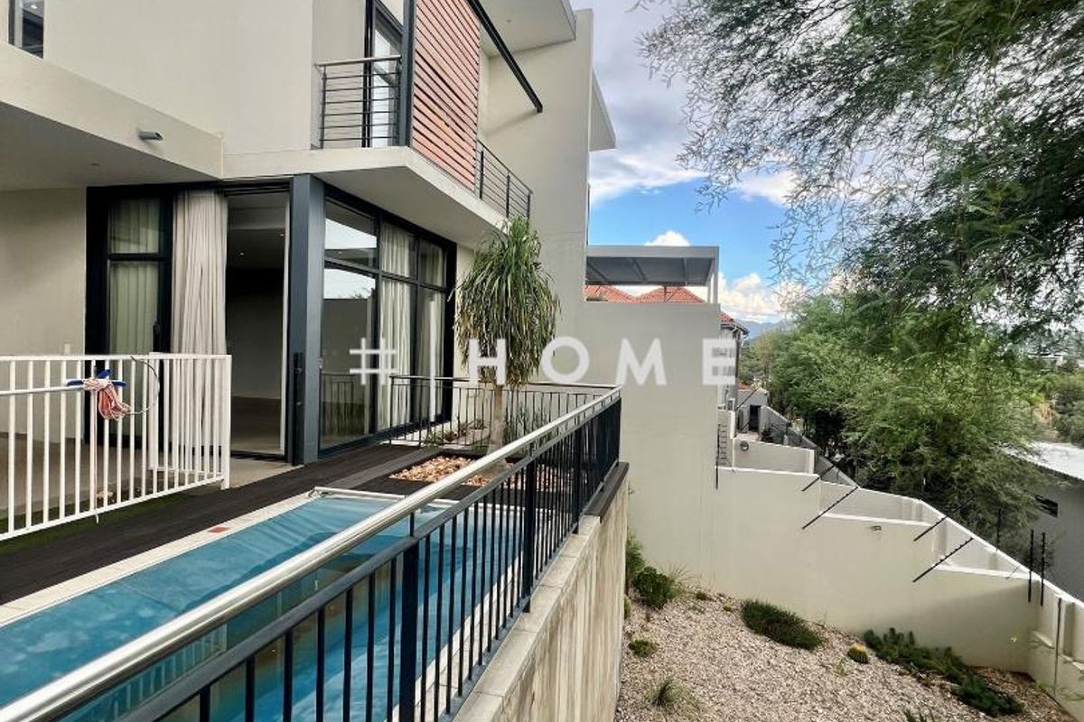 Modern townhouse exterior featuring a raised deck with a lap pool, glass sliding doors, and a landscaped garden area.