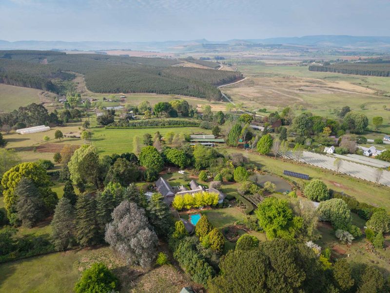 Aerial view of a sprawling farm property featuring a main residence with a swimming pool, solar panels, established gardens, and surrounding agricultural land.