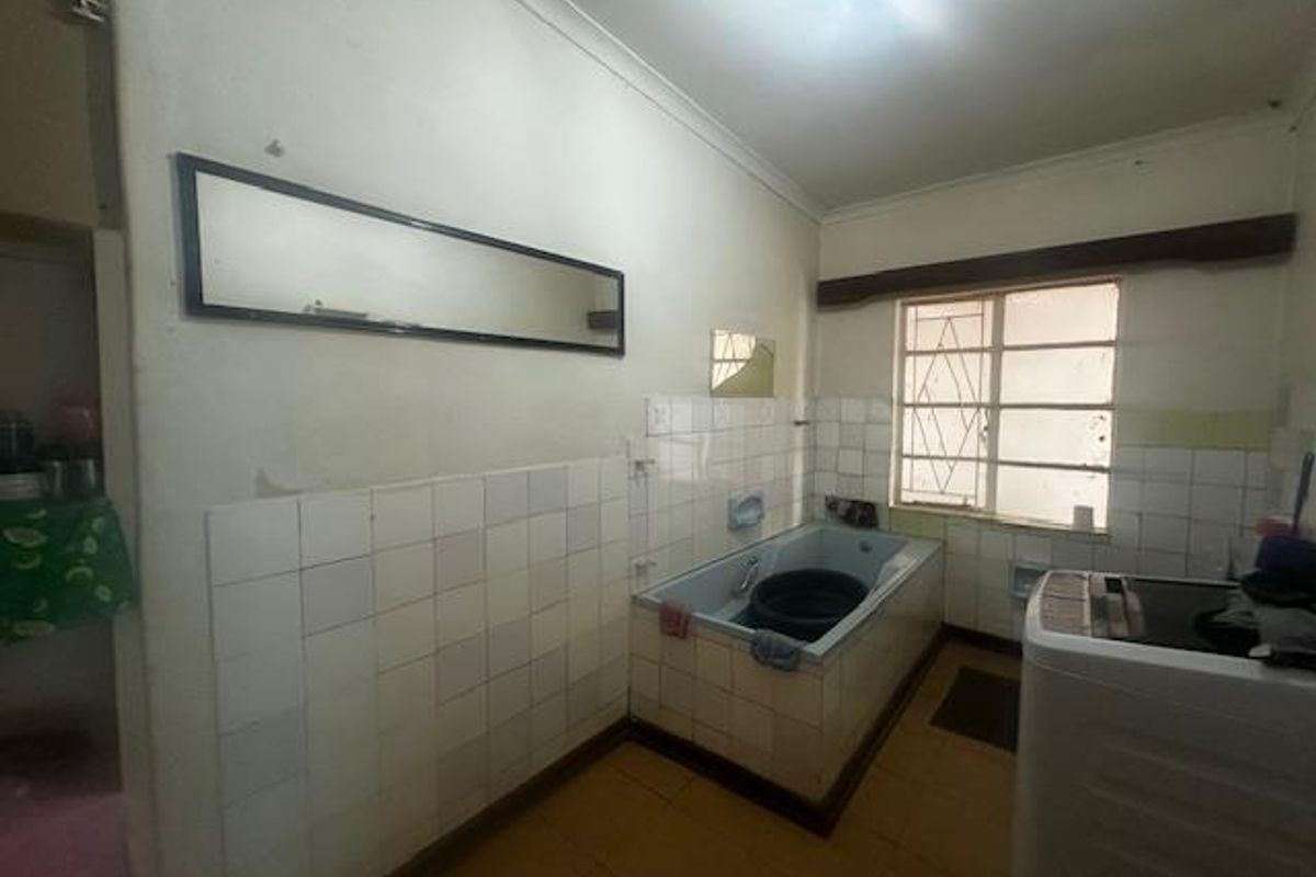 A dated bathroom featuring a built-in tiled bathtub, wall-mounted mirror, and security bars on the window.