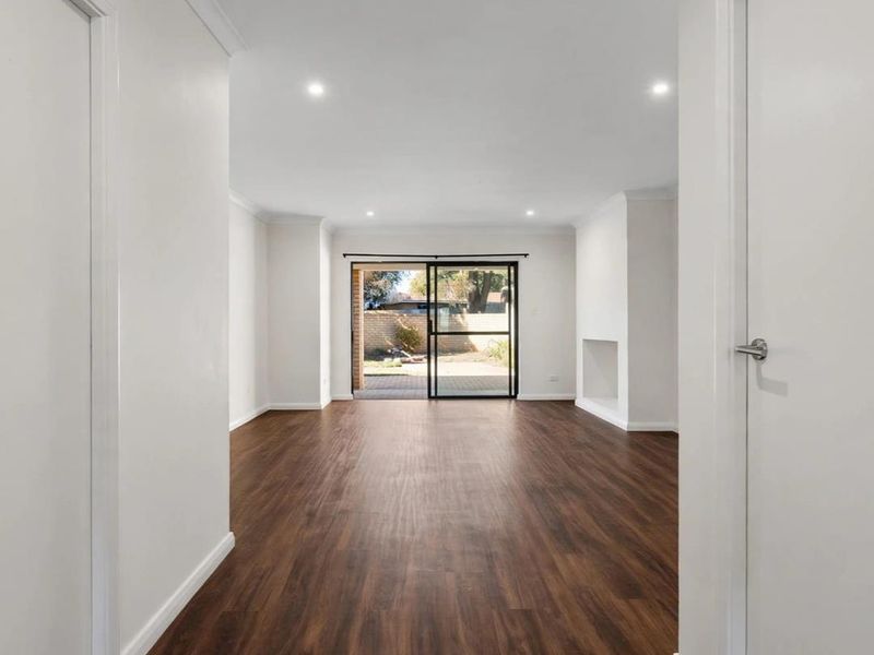 A bright, open-plan living area featuring modern laminate flooring, recessed downlights, and a sliding glass door providing direct access to the rear patio.