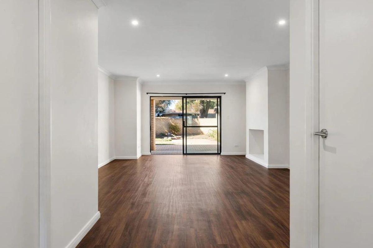 A bright, open-plan living area featuring modern laminate flooring, recessed downlights, and a sliding glass door providing direct access to the rear patio.