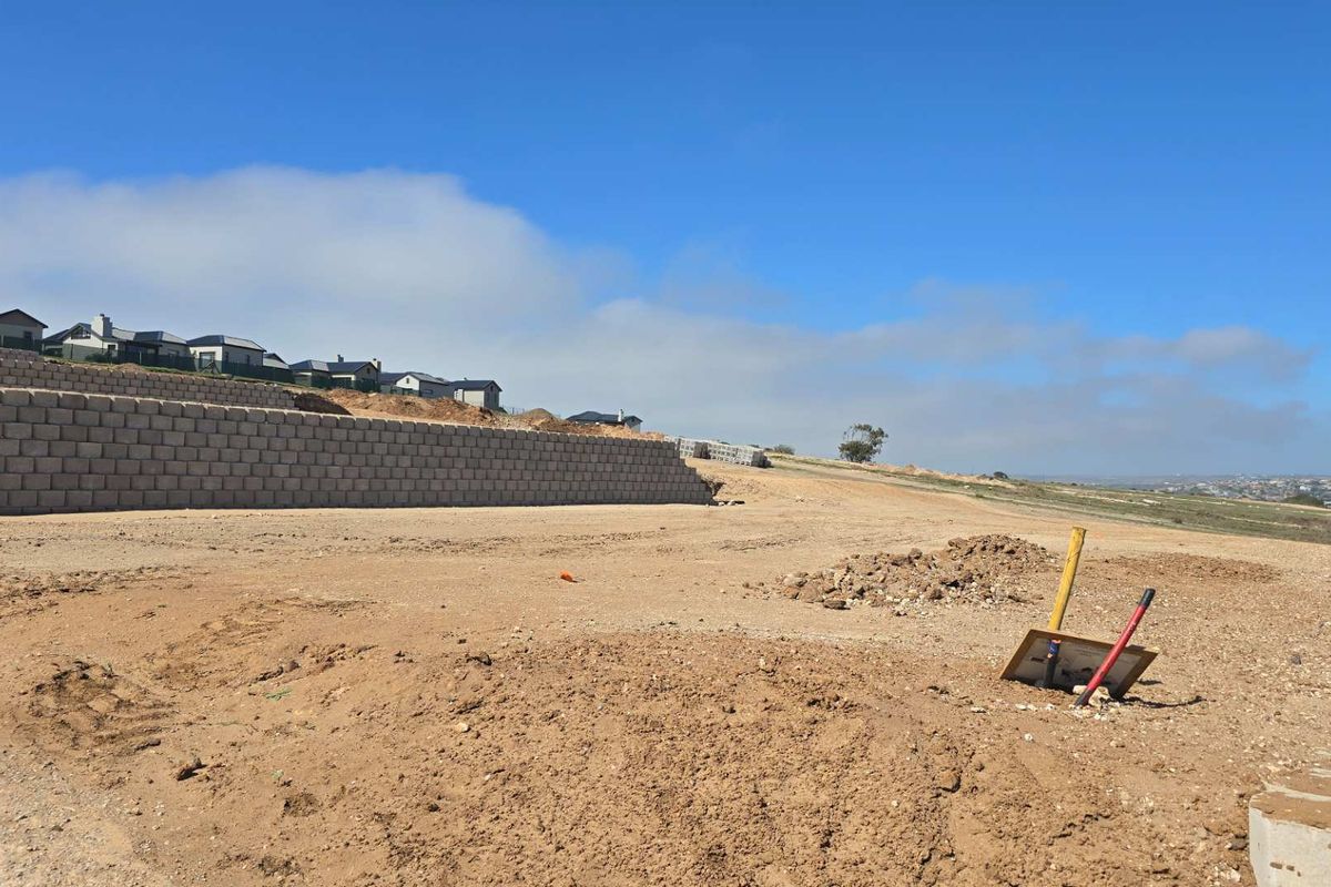 A vacant residential plot featuring a retaining wall and exposed utility connections, ready for development in a scenic estate setting.