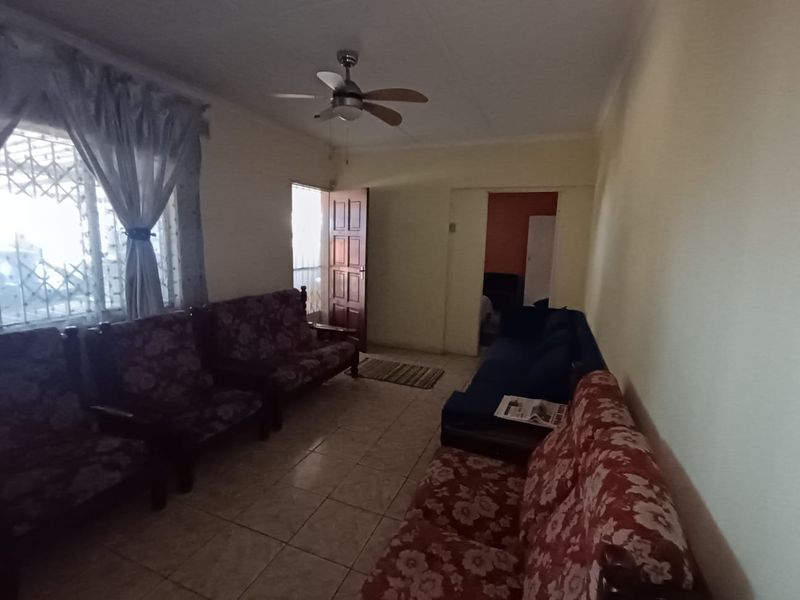 A living room featuring tiled flooring, a ceiling fan, and access to adjacent rooms through a timber door.