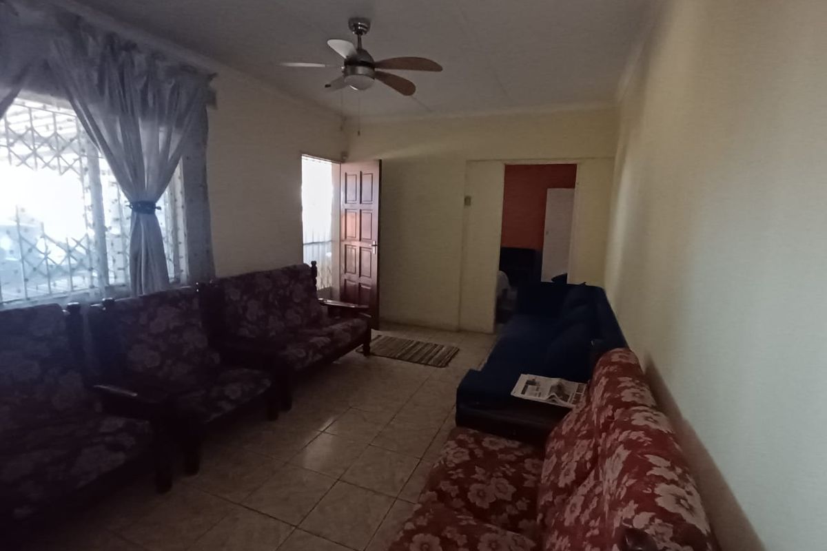 A living room featuring tiled flooring, a ceiling fan, and access to adjacent rooms through a timber door.