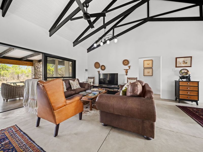 Spacious living room featuring a vaulted ceiling with exposed black timber trusses, polished concrete floors, and large sliding doors opening to the outdoor area.