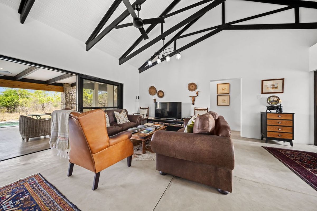 Spacious living room featuring a vaulted ceiling with exposed black timber trusses, polished concrete floors, and large sliding doors opening to the outdoor area.
