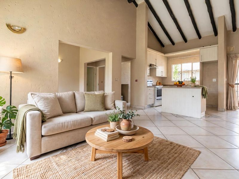 Spacious open-plan living area featuring high vaulted ceilings with exposed timber beams, tiled flooring, and a functional kitchen with built-in cabinetry and island.