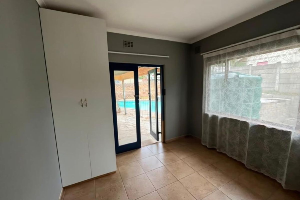 A bright, empty bedroom featuring tiled flooring, a built-in wardrobe, and direct access to the outdoor pool area through a glass door.