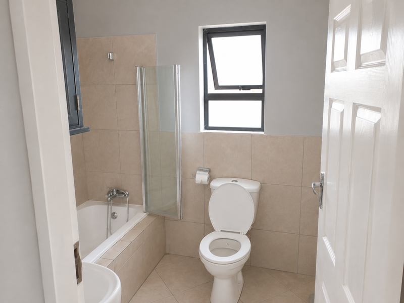 A clean, functional bathroom featuring a bathtub with a glass screen, a standard toilet, and neutral wall and floor tiling.