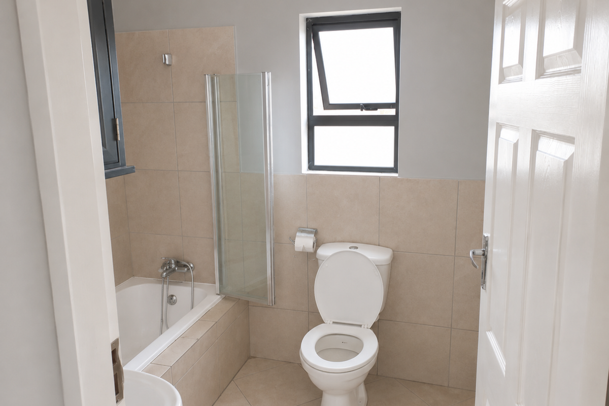 A clean, functional bathroom featuring a bathtub with a glass screen, a standard toilet, and neutral wall and floor tiling.