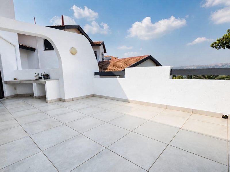 Spacious open-air balcony featuring light-toned floor tiles, a built-in concrete counter, and a parapet wall with views of the surrounding area.