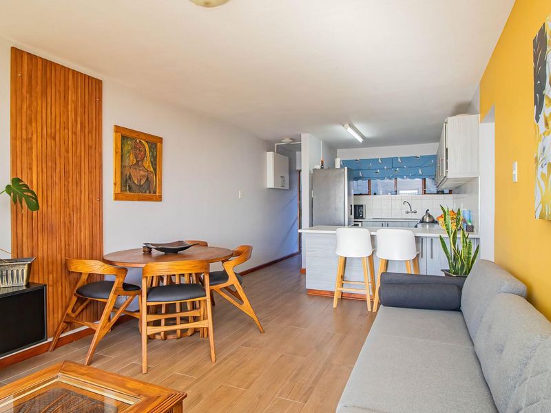 Open-plan living and dining area featuring a compact kitchen with breakfast counter, tiled flooring, and a decorative timber wall feature.