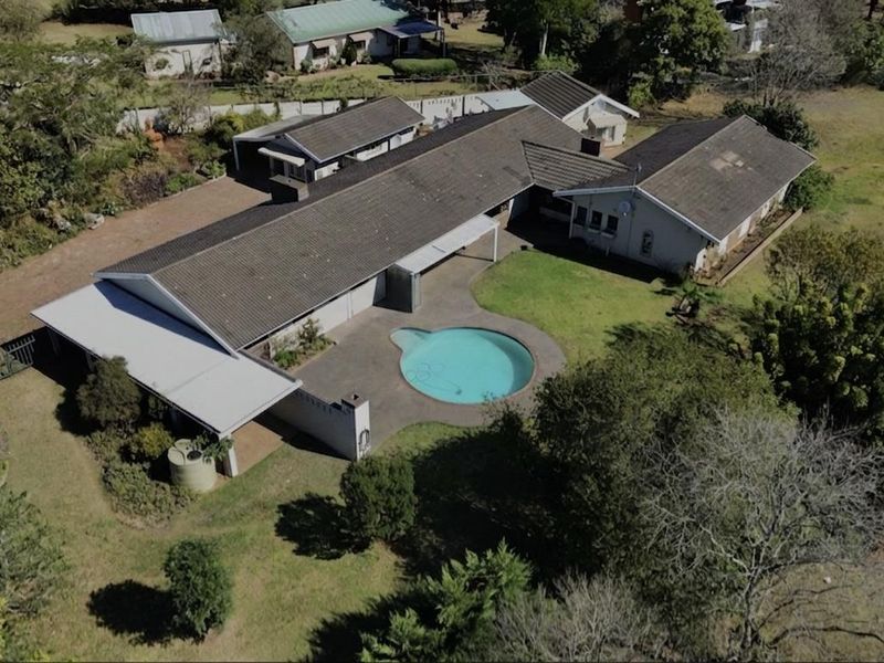 Aerial view of a residential property featuring a swimming pool, expansive garden, paved patio, and a large tiled roof structure.