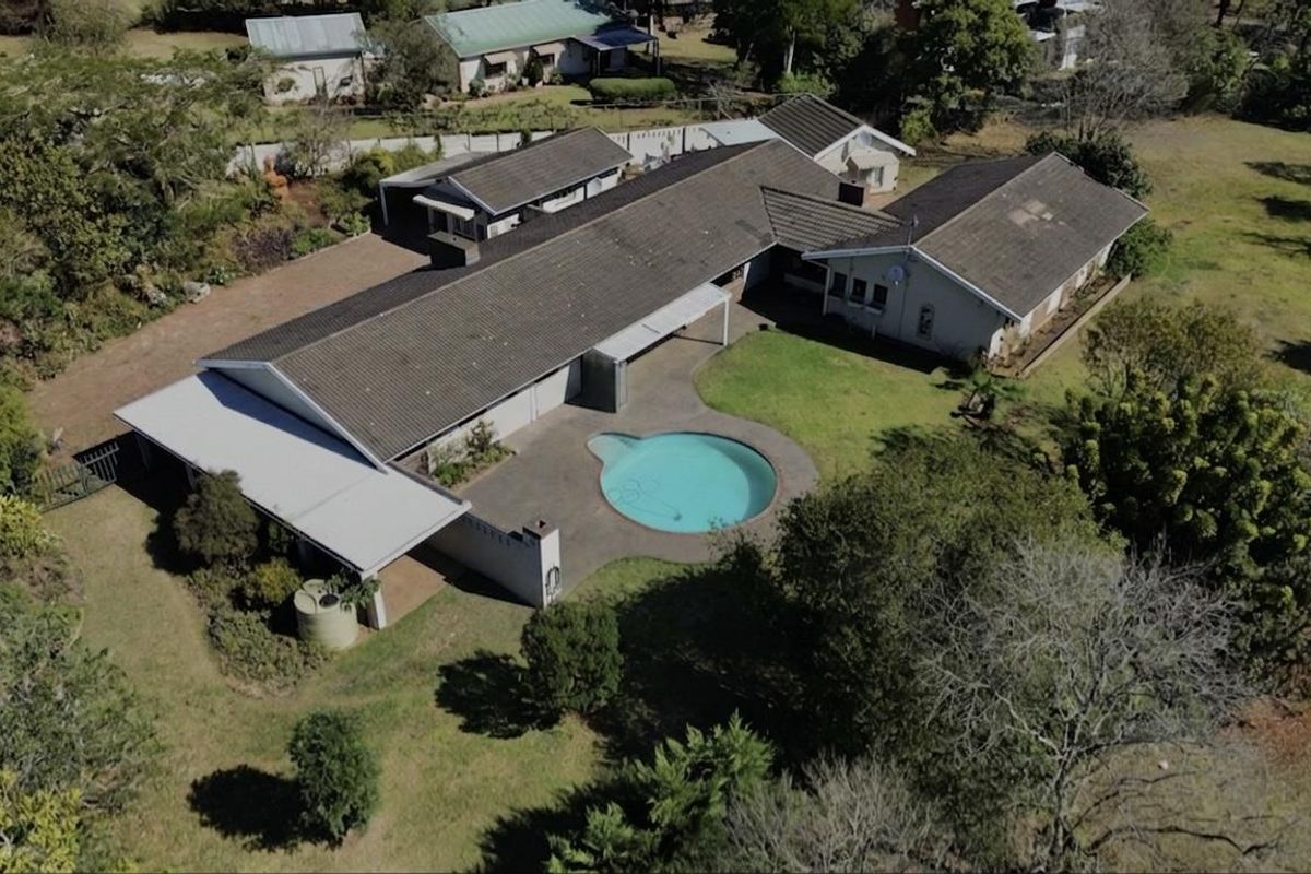 Aerial view of a residential property featuring a swimming pool, expansive garden, paved patio, and a large tiled roof structure.