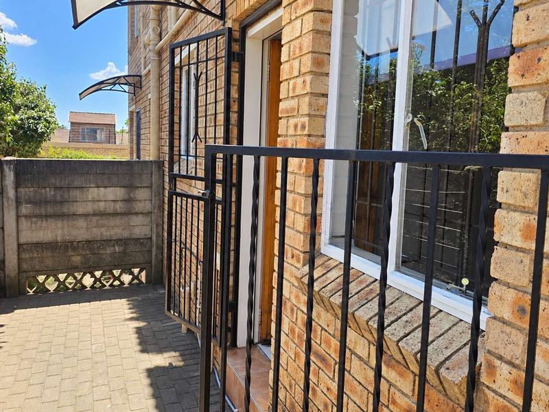 A paved outdoor patio area featuring face brick exterior walls, a security gate, and protective awnings, providing a functional and secure entrance space.