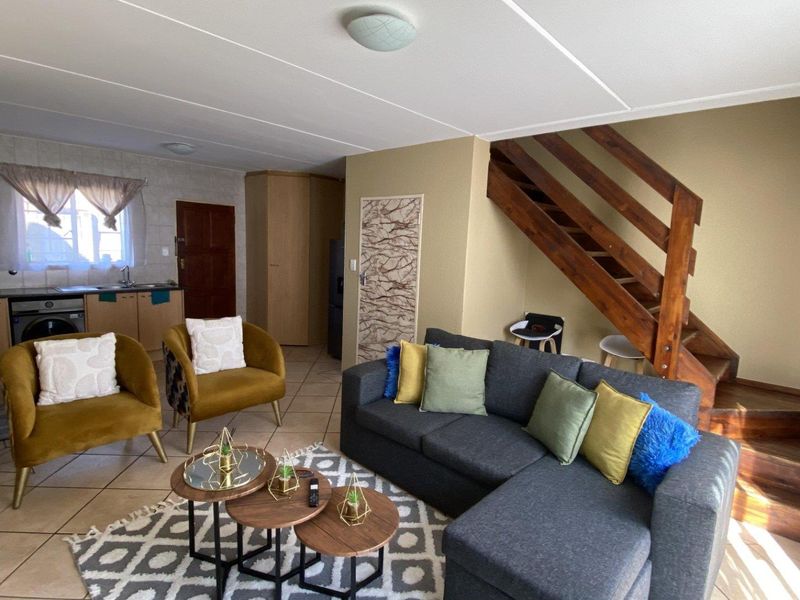 Open-plan living area featuring tiled flooring, a functional kitchen space, and a wooden staircase leading to the upper level.