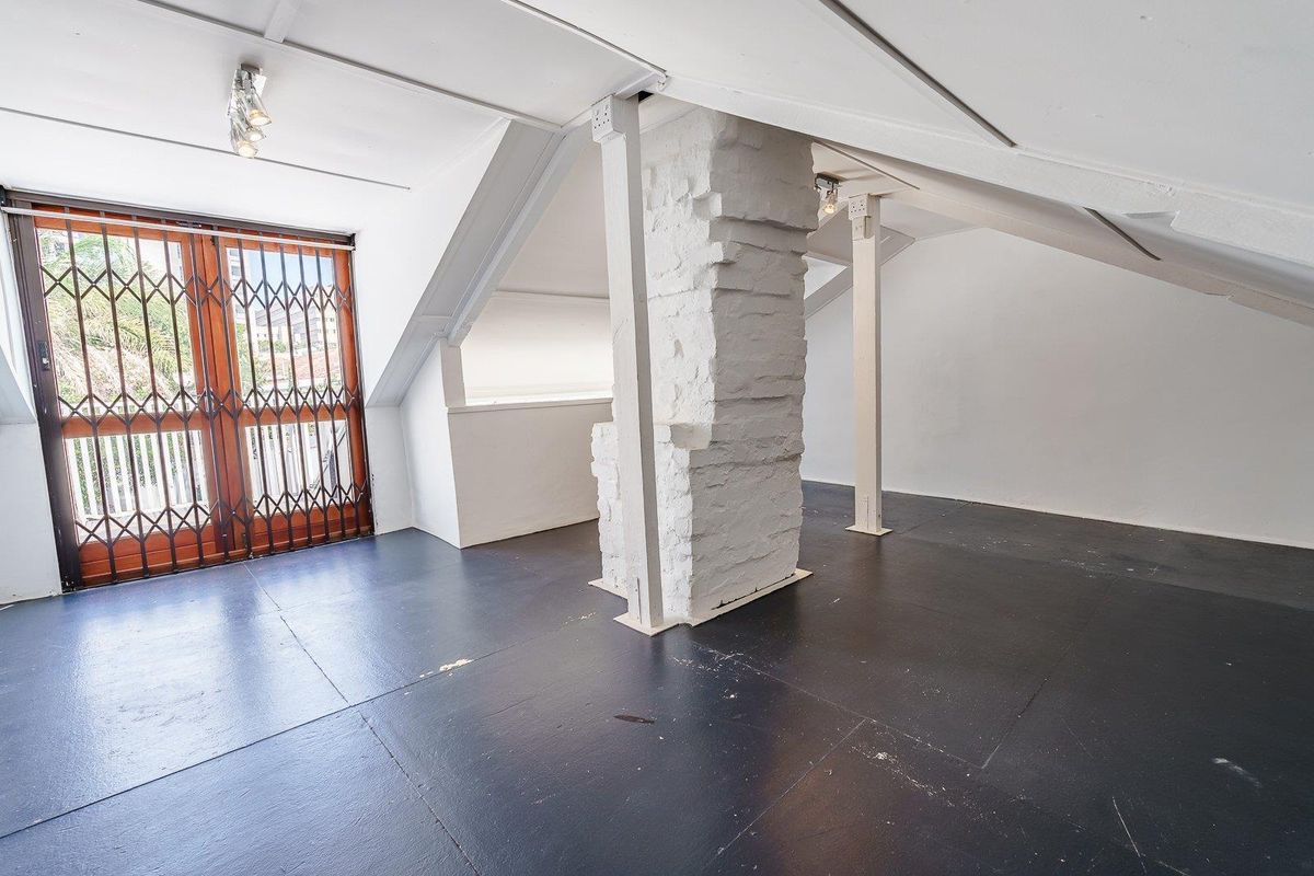 An attic-style bedroom or living space featuring a pitched ceiling, exposed structural pillar, and access to a balcony through a security gate.