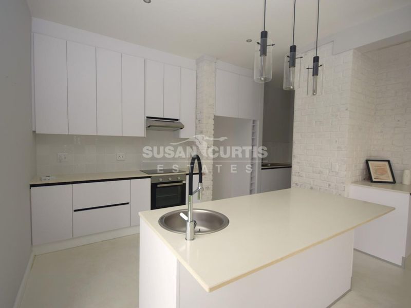 Modern kitchen featuring white cabinetry, a central island with an integrated sink, built-in appliances, and a stylish exposed brick feature wall.
