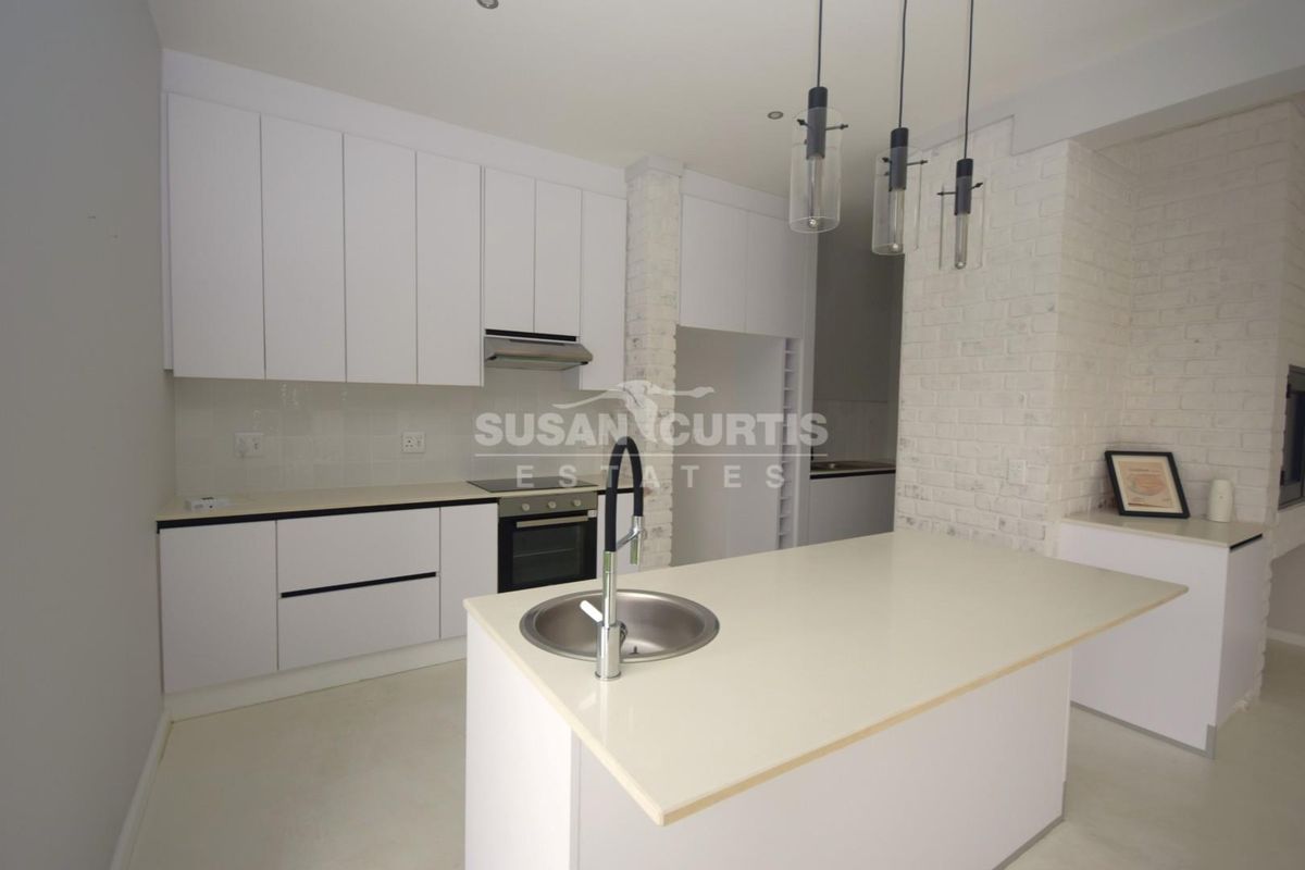Modern kitchen featuring white cabinetry, a central island with an integrated sink, built-in appliances, and a stylish exposed brick feature wall.