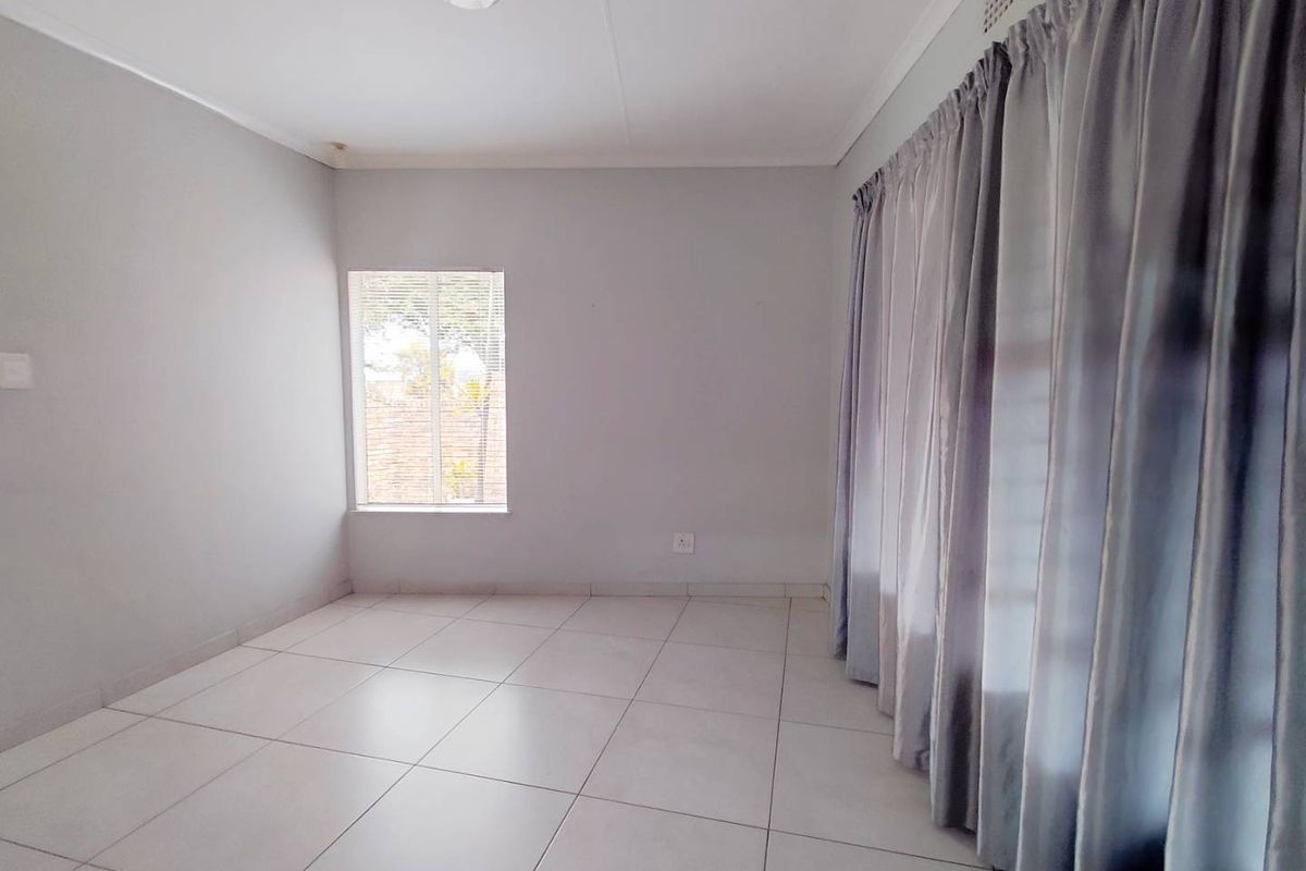 A bright, empty bedroom featuring neutral tiled flooring, clean walls, and a large window with curtains, offering a blank canvas for personalization.