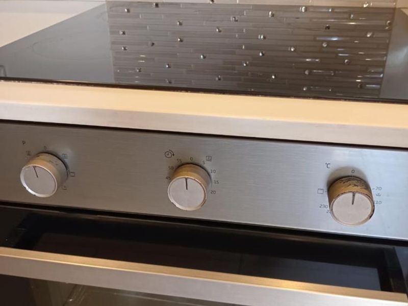Close-up view of a stainless steel built-in oven and electric hob with a decorative tiled backsplash.