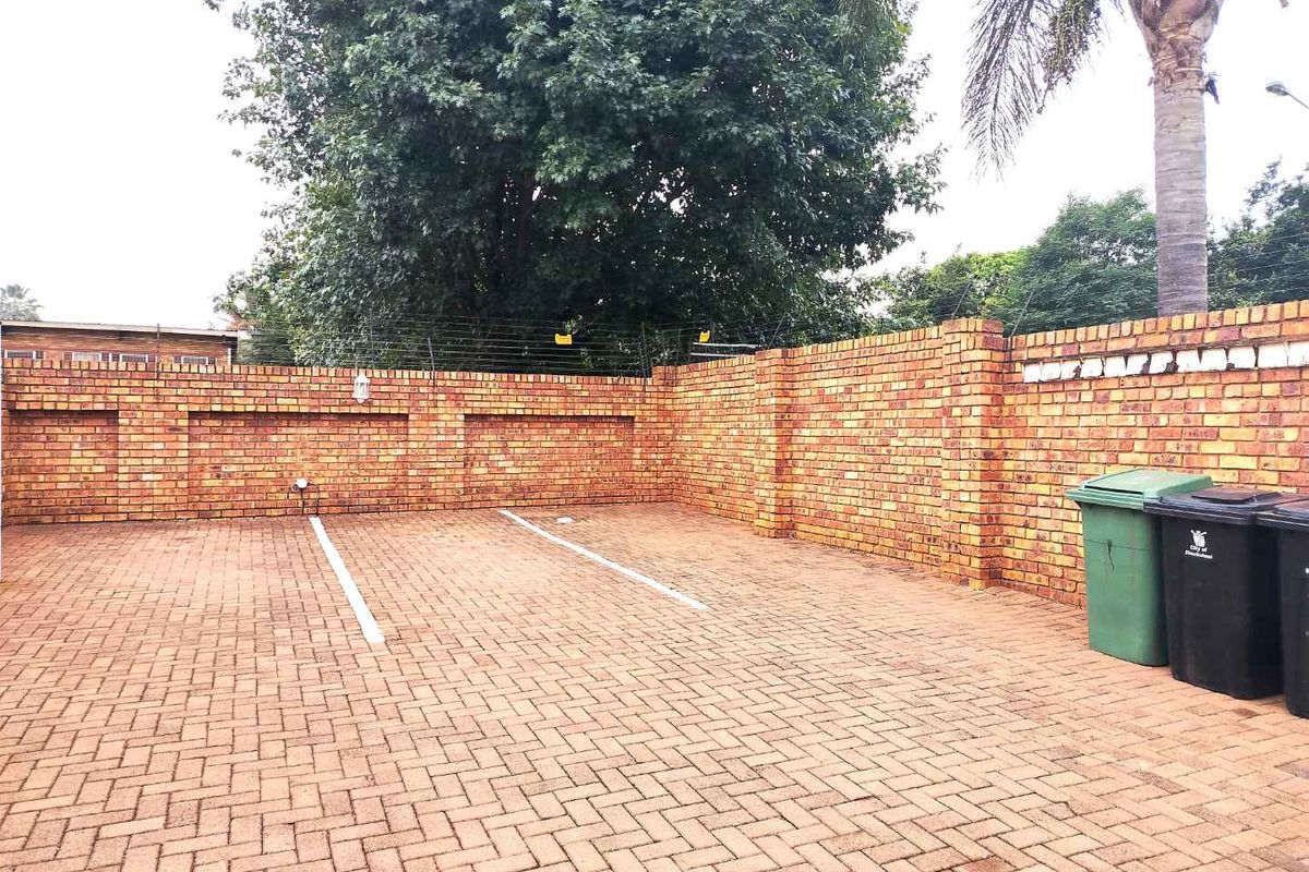 A paved outdoor parking area featuring high perimeter brick boundary walls with integrated electric fencing and marked parking bays.