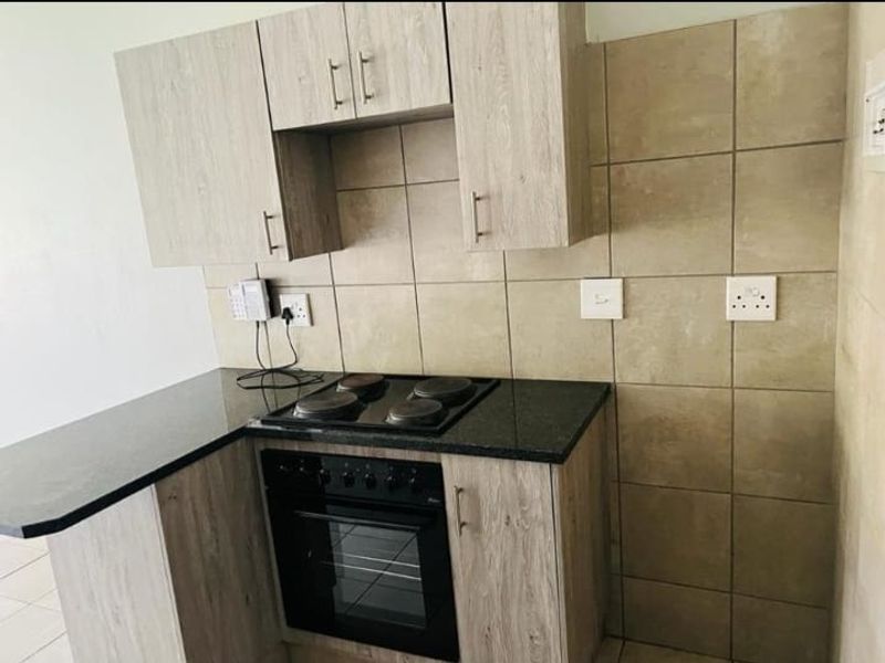 Compact kitchen featuring light wood-grain cabinetry, dark granite countertops, a built-in electric oven and hob, and neutral tiled backsplash.