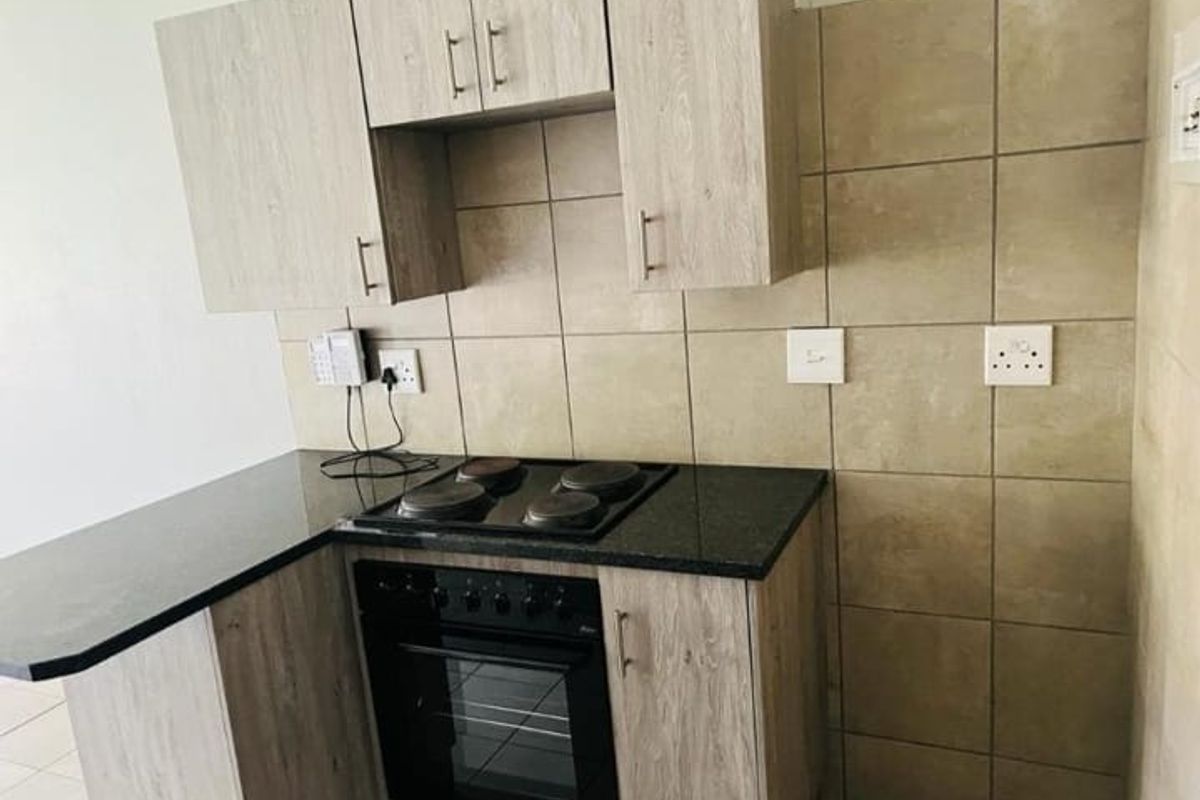 Compact kitchen featuring light wood-grain cabinetry, dark granite countertops, a built-in electric oven and hob, and neutral tiled backsplash.