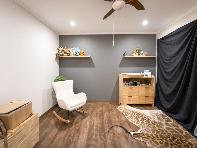 A well-maintained bedroom featuring modern laminate flooring, recessed lighting, a ceiling fan, and two floating shelves against a dark accent wall.