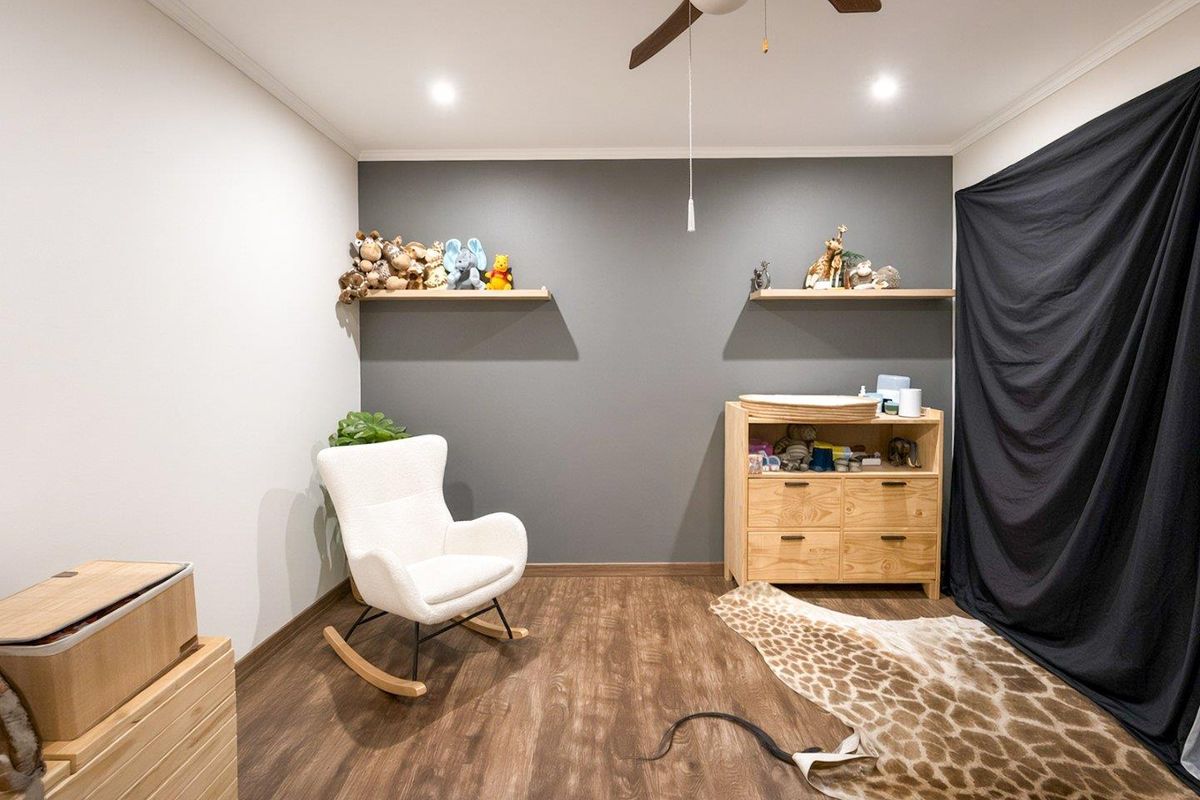A well-maintained bedroom featuring modern laminate flooring, recessed lighting, a ceiling fan, and two floating shelves against a dark accent wall.