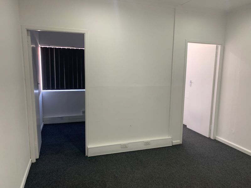 A vacant office space featuring dark carpeting, white walls, and multiple doorways leading to adjacent rooms, providing a clean and functional workspace.