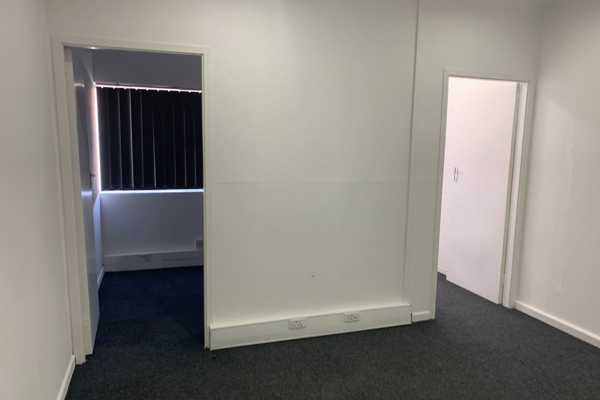 A vacant office space featuring dark carpeting, white walls, and multiple doorways leading to adjacent rooms, providing a clean and functional workspace.