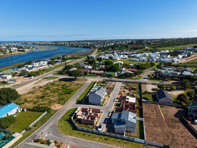 Aerial view of a coastal residential development featuring ongoing construction, paved access roads, and proximity to the river and surrounding neighborhood.