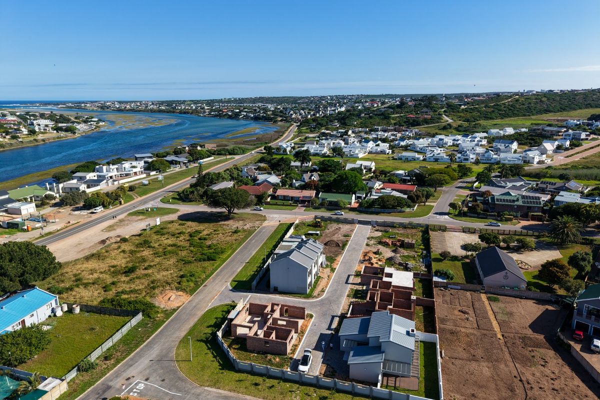 Aerial view of a coastal residential development featuring ongoing construction, paved access roads, and proximity to the river and surrounding neighborhood.