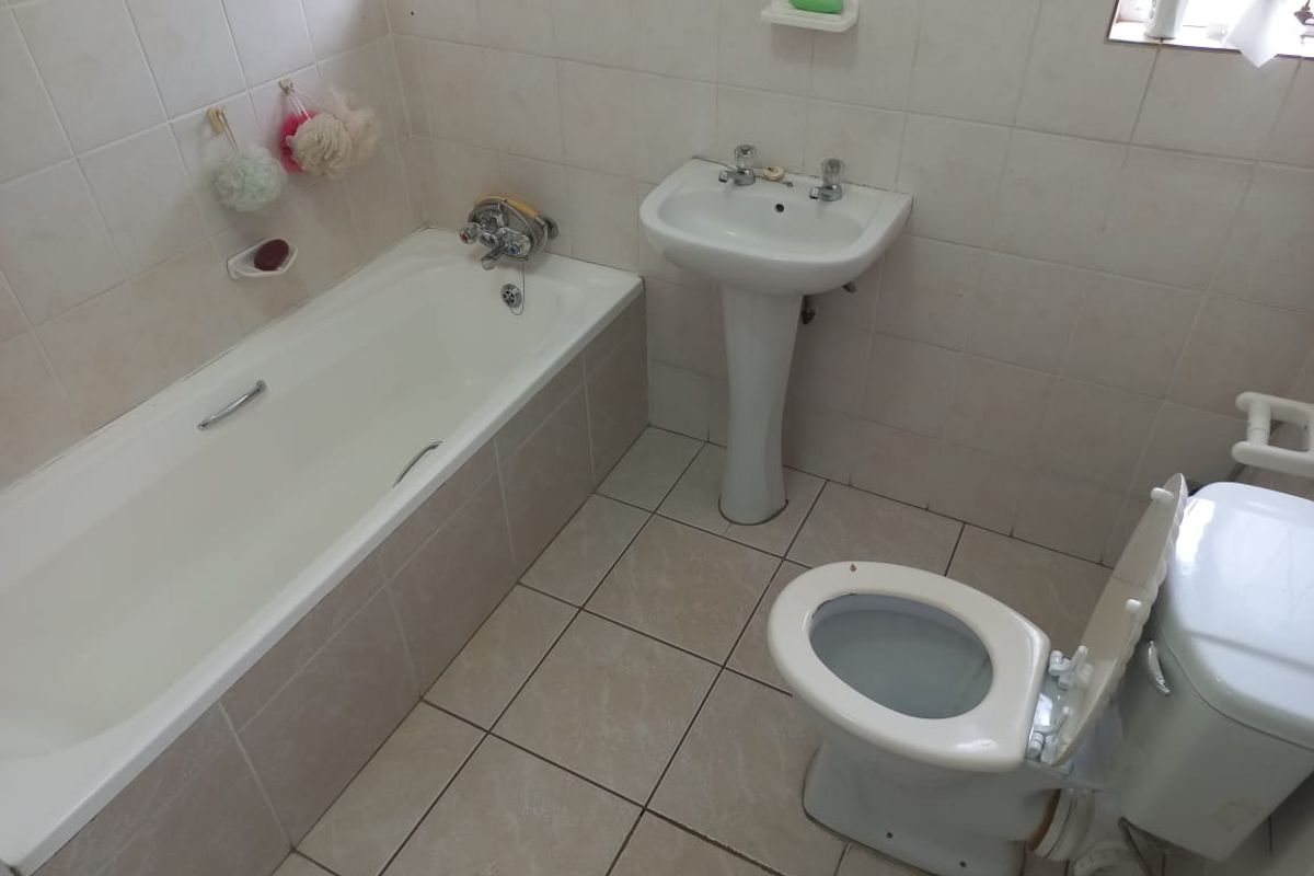 A functional bathroom featuring a standard bathtub, pedestal washbasin, and toilet with neutral ceramic wall and floor tiling.
