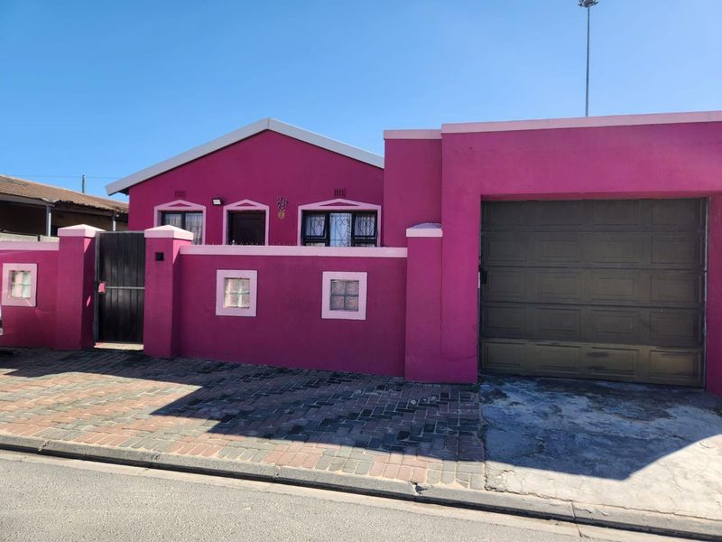 Front elevation of a residential property featuring a vibrant pink facade, secure boundary wall, pedestrian gate, and an integrated garage.